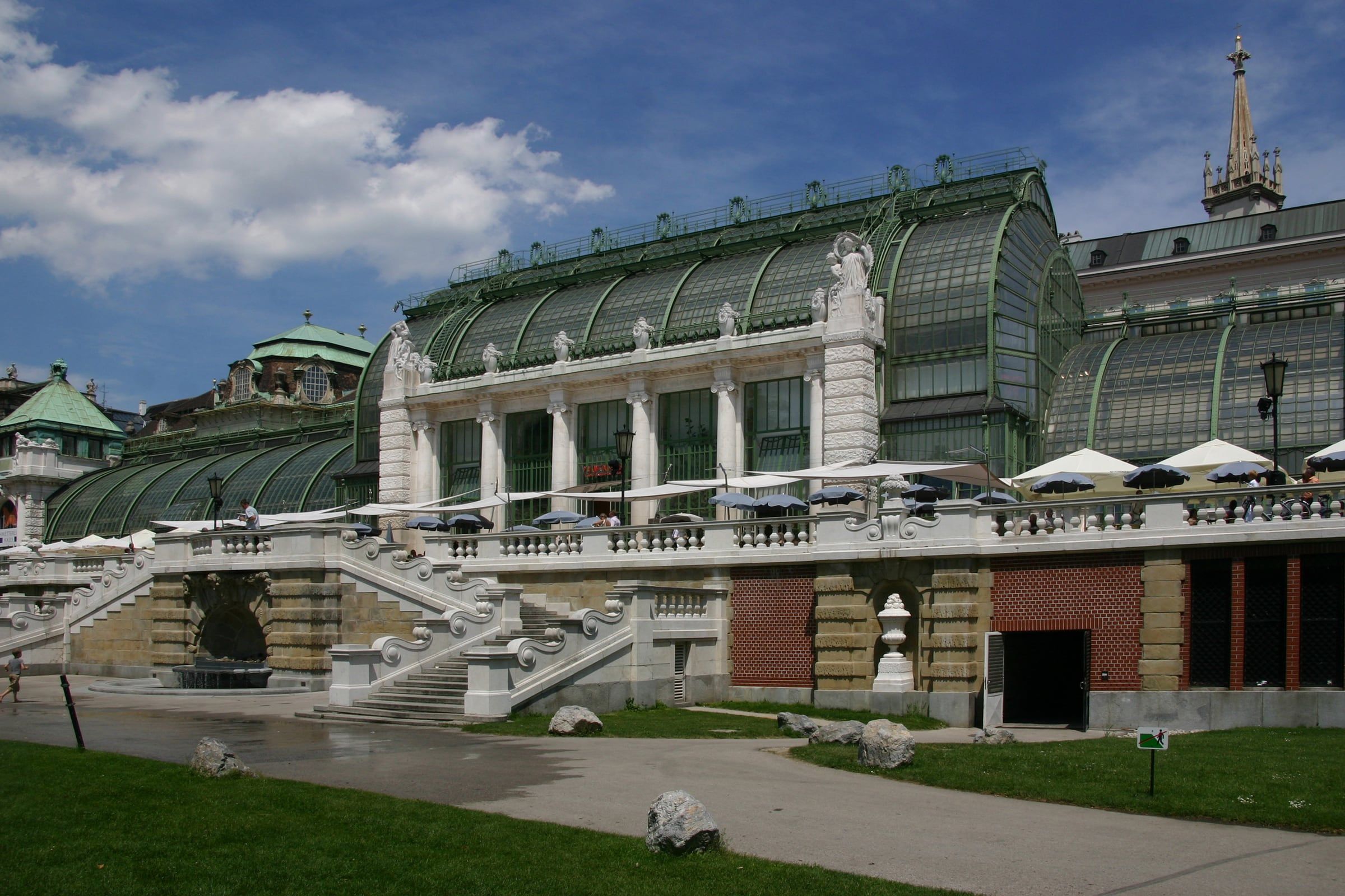 The glasshouse of the Palmenhaus in the Burggarten, with its green iron and glass roof, stone balustrades and steps in front.